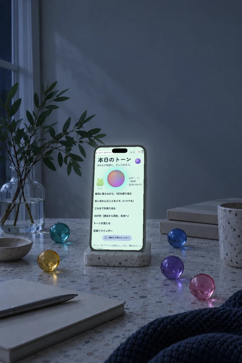 夜の机の上、スタンドに立てたスマートフォン。暗い部屋で、本日のトーンのホーム画面が光っている